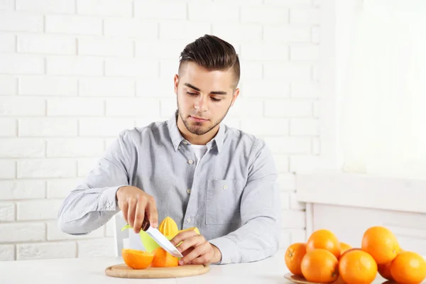 Молодий чоловік ріже апельсин, готуючи апельсиновий сік — стокове фото