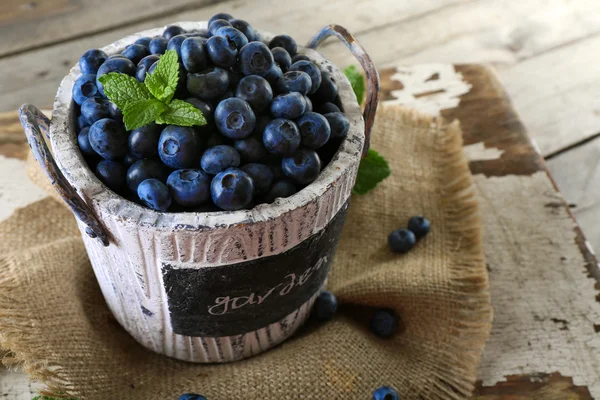 Tasty ripe blueberries with green leaves in bucket on table close up — Stock Photo, Image