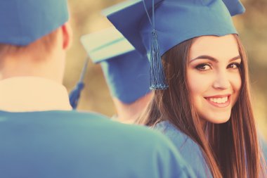 Graduated students in graduation hats and gowns, outdoors clipart