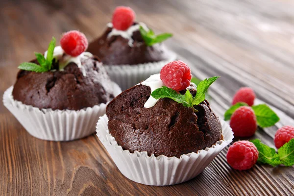 Deliciosos cupcakes de chocolate com bagas e hortelã fresca na mesa de madeira fechar — Fotografia de Stock