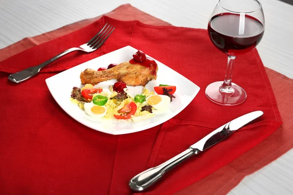 Kadeh şarap peçete, closeup tablo ile beyaz tabak içinde pişmiş tavuk bacak ve sebze salatası fincan — Stok fotoğraf