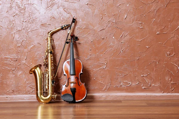 Saxofone e violino na parede marrom — Fotografia de Stock