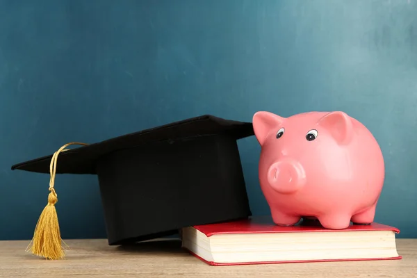 Piggy bank with book and grad hat — Stock Photo, Image