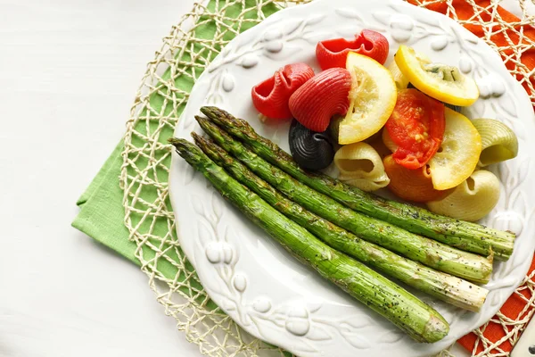 Asparagi arrosto e gustosa pasta colorata con verdure su piatto su fondo tavola in legno — Foto Stock