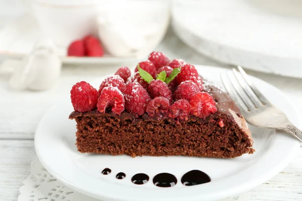 Stück Kuchen mit Schokoladenglasur und Himbeeren auf farbigem Holzhintergrund — Stockfoto