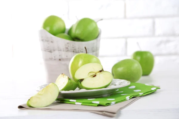 Gröna äpplen i tefat på bord med servett på vitt tegel vägg bakgrund — Stockfoto