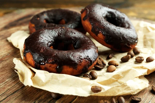 Delicious doughnuts with chocolate icing and coffee beans on table close up — Stock Photo, Image