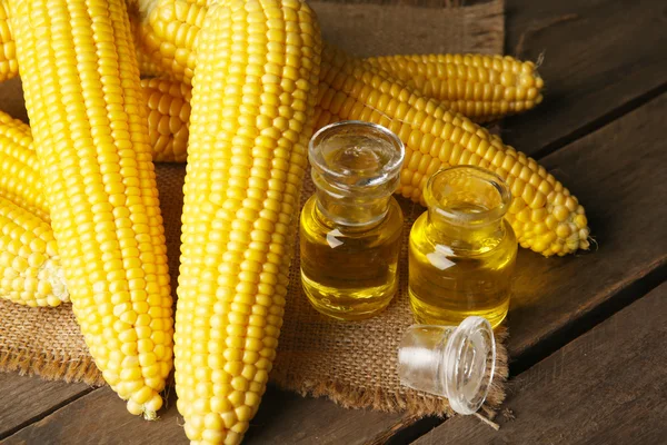 Fresh corn with bottles of oil on table close up