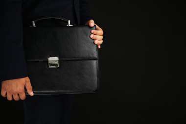 Koyu arka plan üzerinde evrak çantası ile takım elbiseli şık adam