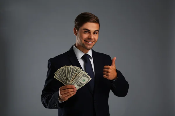 Elegante uomo in giacca e cravatta in possesso di denaro su sfondo grigio — Foto Stock