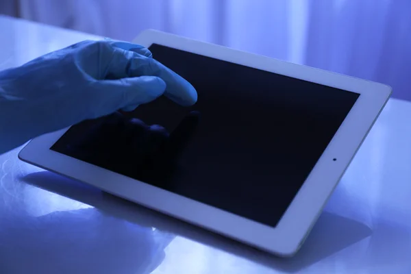 Main de médecin en gant de caoutchouc à l'aide d'une tablette au bureau — Photo