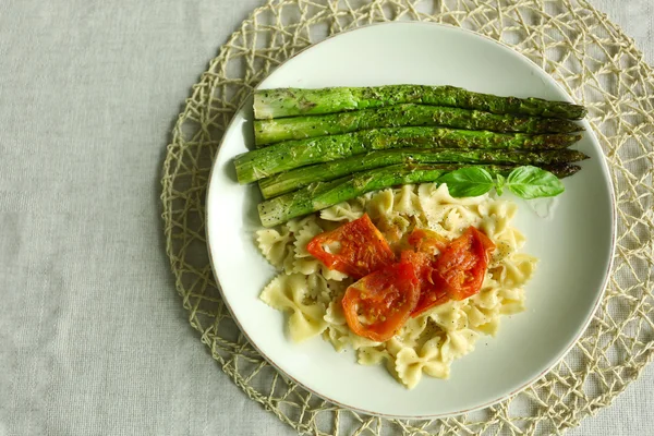 Roasted asparagus and tasty pasta with vegetables on plate on wooden table background — Stock Photo, Image