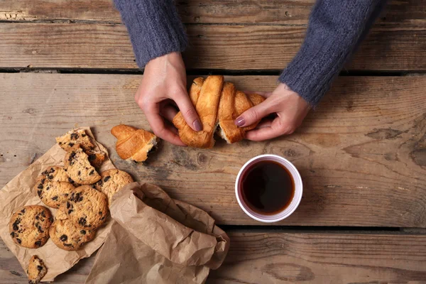 Female hands holding cup of coffee and cookies on wooden table close up — Stock Photo, Image