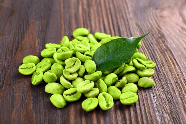 Grüne Kaffeebohnen mit Blatt auf Holzgrund — Stockfoto