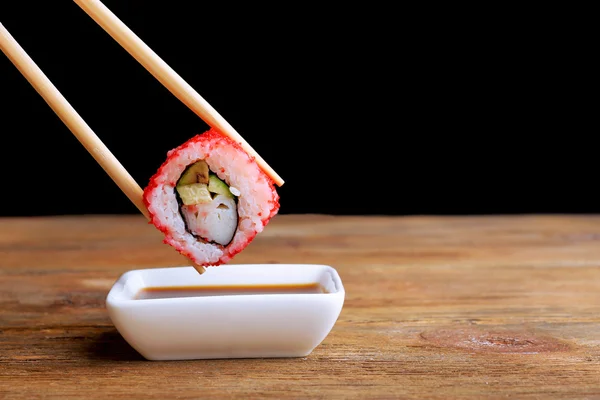 Dipping roll in sauce on dark background — Stock Photo, Image