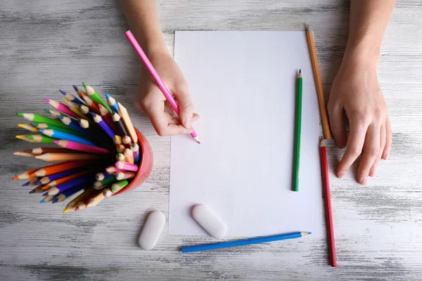 Hand met kleur potloden en blanco vel papier op houten tafel — Stockfoto