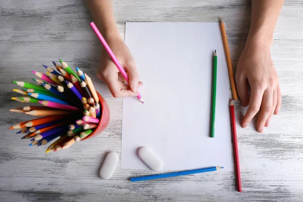 Hand with color pencils and blank sheet of paper on wooden table — Stock Photo, Image