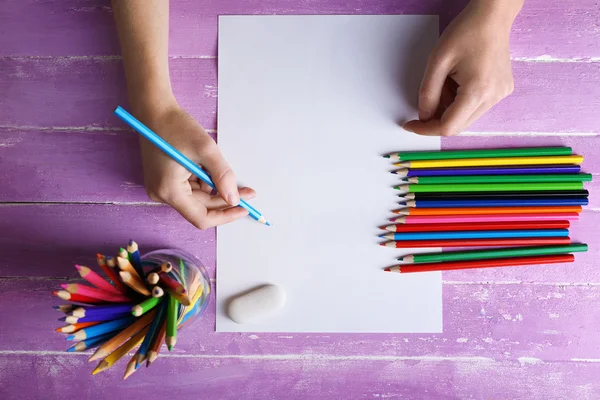 Mano con lápices de color y hoja de papel en blanco sobre mesa de madera —  Fotos de Stock