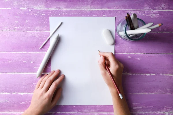 Mano con lápices de color y hoja de papel en blanco sobre mesa de madera —  Fotos de Stock