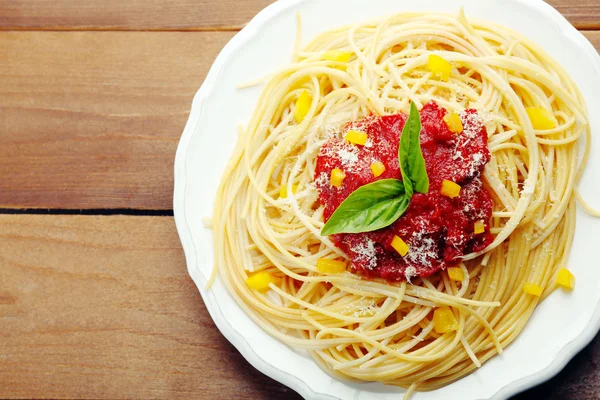 Spaghetti mit Tomatensauce, Paprika und Käse auf weißem Teller, auf farbigem Holzhintergrund — Stockfoto