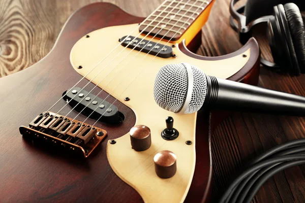 Electric guitar with microphone and headphones on wooden table close up — Stock Photo, Image
