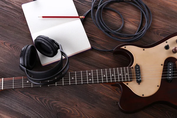 Electric guitar with headphones and notebook on wooden table close up — Stock Photo, Image