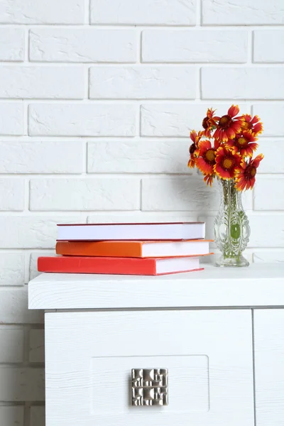 Hermosas flores con libros sobre fondo de pared de ladrillo — Foto de Stock