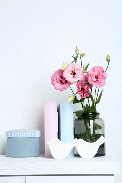 Beautiful flowers in vase with books on wall background — Stock Photo, Image