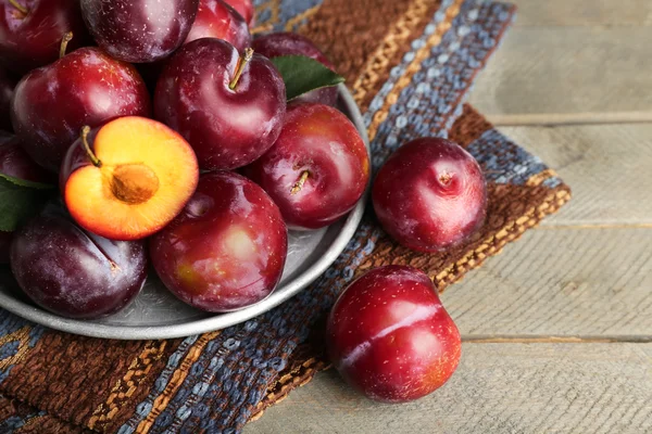 Ripe plums in metal plate on wooden table, closeup — Stock Photo, Image