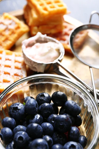 Sweet homemade waffles and blueberries on tray, on color wooden background — Stock Photo, Image