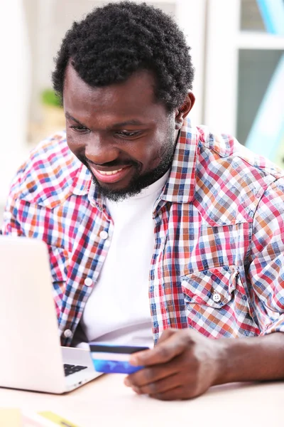 Hombre afroamericano con portátil y tarjeta de crédito en el lugar de trabajo —  Fotos de Stock