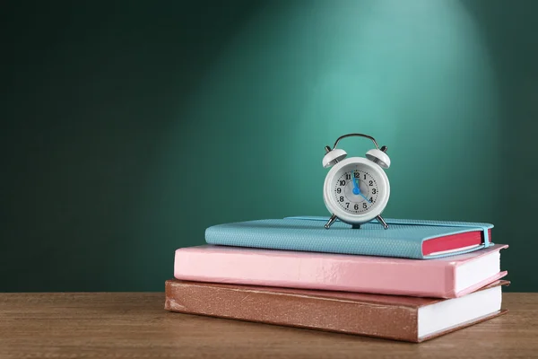 Stapel boeken met wekker op Bureau op groene schoolbord achtergrond — Stockfoto