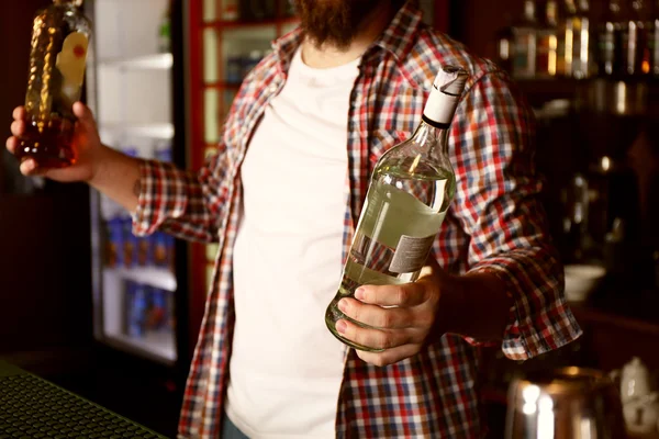 Portrait de beau barman tenant des bouteilles avec des boissons alcoolisées — Photo