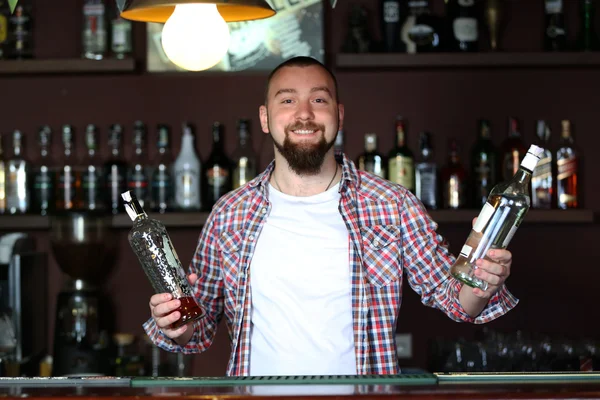 Portrait de beau barman tenant des bouteilles avec des boissons alcoolisées — Photo