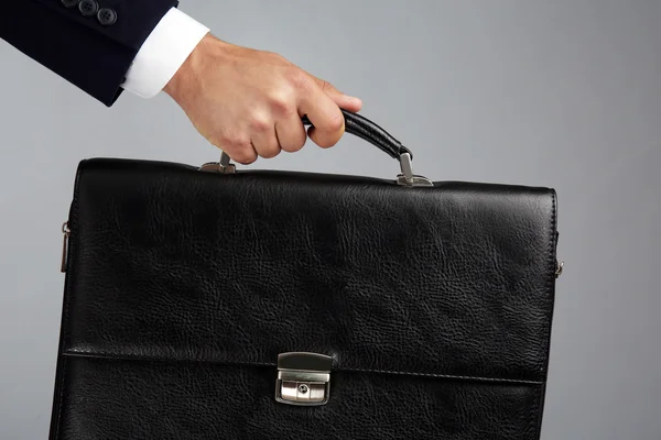 Male hand holding briefcase on gray background — Stock Photo, Image