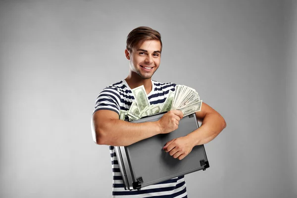 Guapo joven sosteniendo caso con dinero sobre fondo gris — Foto de Stock