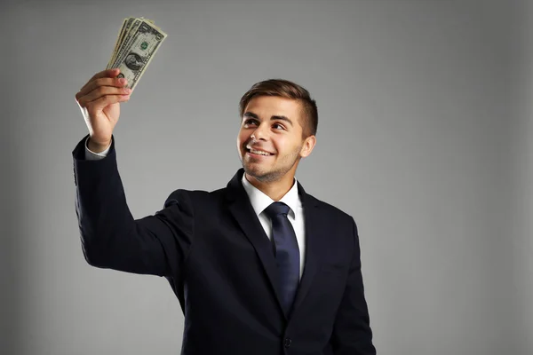 Homem elegante em terno segurando dinheiro em fundo cinza — Fotografia de Stock
