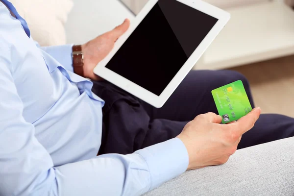 Man holding credit card and tablet on sofa in room — Stock Photo, Image