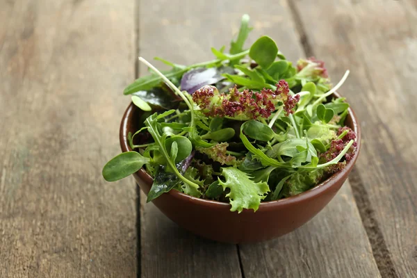 Fresh mixed green salad in bowl on wooden table close up — Stock Photo, Image