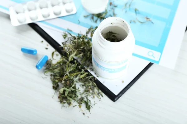 Bottle of dry medical cannabis and pills with clipboard on table close up — Stock Photo, Image