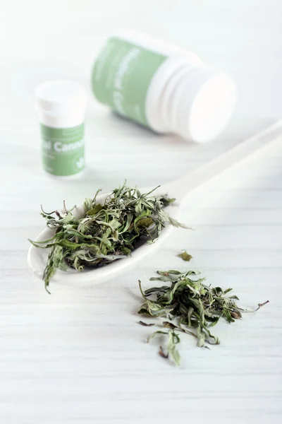 Bottle of medical cannabis with dry herbs in spoon on table close up — Stock Photo, Image