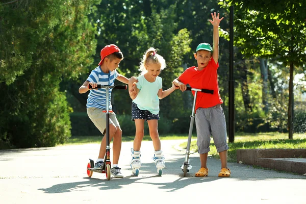 Children riding on scooters and roller skates — Stock Photo, Image
