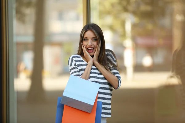 Mooie jonge vrouw met shopping tassen in de buurt van vitrines buiten — Stockfoto