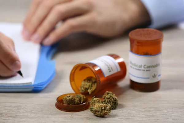 Médico escrevendo sobre prescrição em branco e garrafa com cannabis medicinal na mesa de perto — Fotografia de Stock