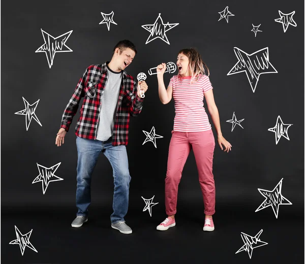 Funny young couple singing together with microphones, on black background — Stock Photo, Image