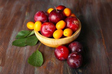 Ahşap arka plan üzerinde kapta olgun Erik