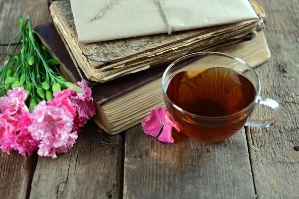 Stare książki z pięknymi kwiatami i filiżankę herbaty na drewnianym stole z bliska — Zdjęcie stockowe