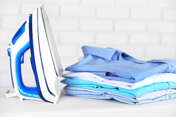 Electronic ironing and pile of clothes on board on brick wall background — Stock Photo, Image