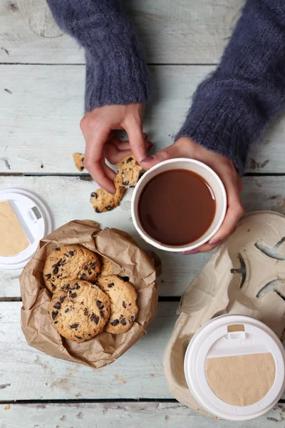 Female hands holding cup of coffee and cookies on wooden table close up — Stock Photo, Image