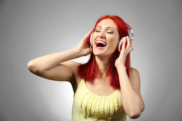 Mulher bonita com fones de ouvido no fundo cinza — Fotografia de Stock